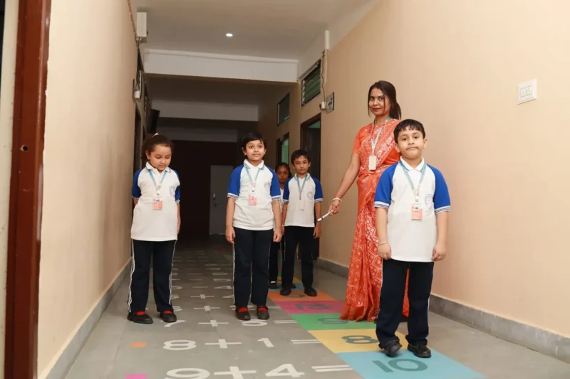 A teacher guiding small children over the number game painted on the corridor floor